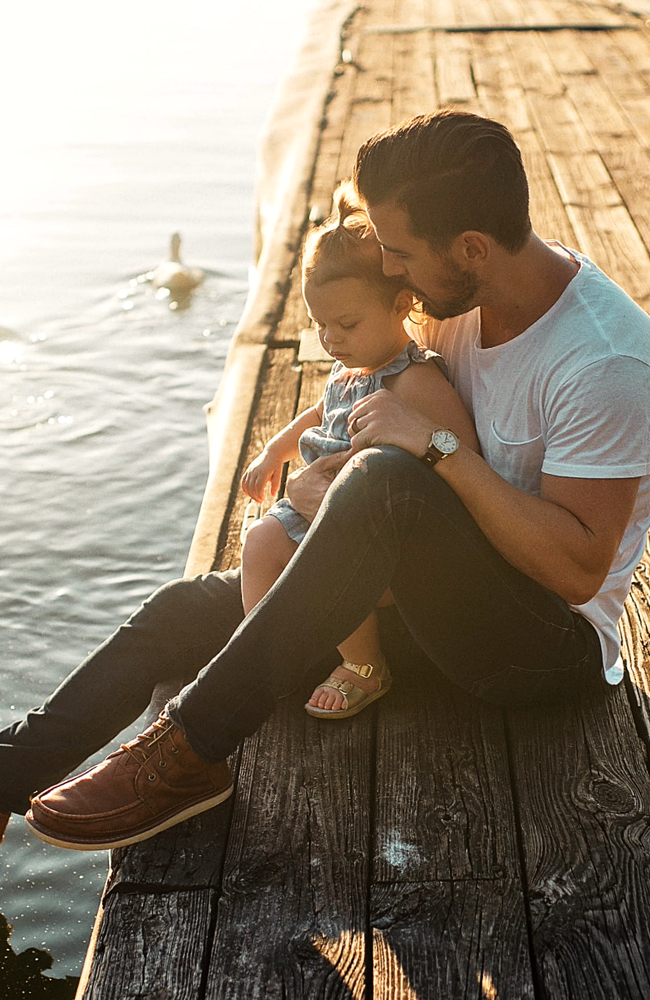 Foto eines jungen Mannes mit seiner Tochter im Arm am Wasser