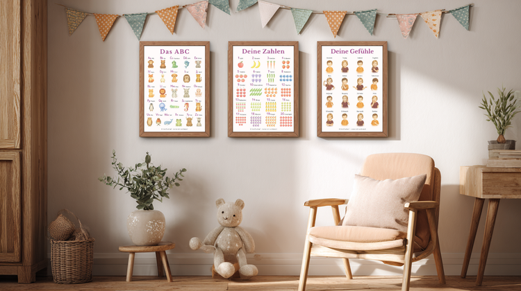 Kinderzimmer im skandinavischen Stil mit drei liebevoll illustrierten Kinderpostern in Holzrahmen – Emotionenrad, Tieralphabet und Affirmationskreis – dekoriert mit bunter Stoffgirlande, Kuschelbär, Pflanze und Holzstuhl in warmer, natürlicher Atmosphäre.