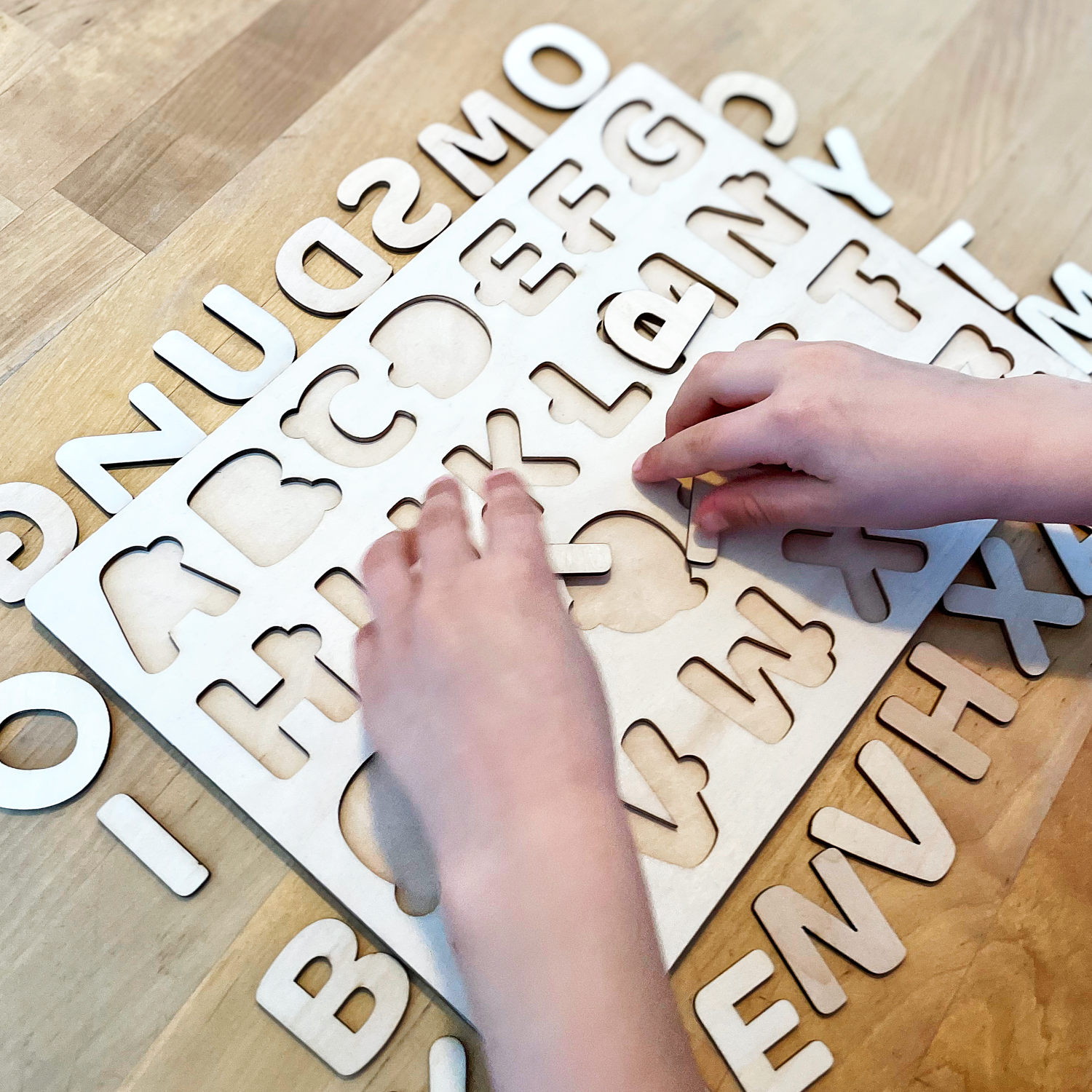 Kinderhänder benutzen eine Holztafel mit herausnehmbaren Buchstaben.